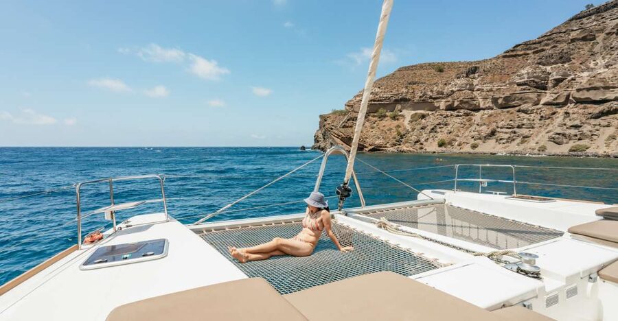 A catamaran under sail below the Santorini caldera cliffs